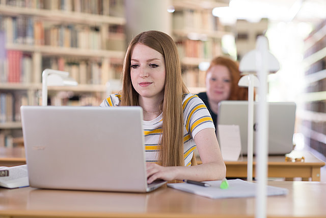 Studierende in Bibliothek mit Laptop