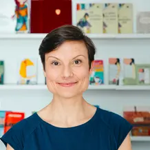 Eine l&auml;chelnde Frau mit kurzen, glatten Haaren vor einem B&uuml;cherregal.