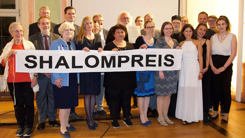 Preisträger Pfarrer Jozsef Lanko (Bildmitte mit Urkunde), links davor Agnes Jovanovic (Kindergartenleiterin im Projekt), Barbara Loos (Vorsitzende des Hochschulrates der KU; 3.v.l.),  Gerhard Rott (Leiter des Referates Weltkirche des Bistums Eichstätt; 2.v.l.), dahinter Burkhard Haneke (Geschäftsführer von Renovabis), daneben Schirmherr OB Andreas Steppberger. (Foto: AK Shalom)