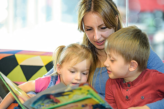 Frau schaut mit Kindern ein Buch an