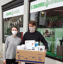 Zwei Menschen mit Maske vor einer Apotheke. Der Mann trägt einen Karton mit Spenden für die Ukraine.