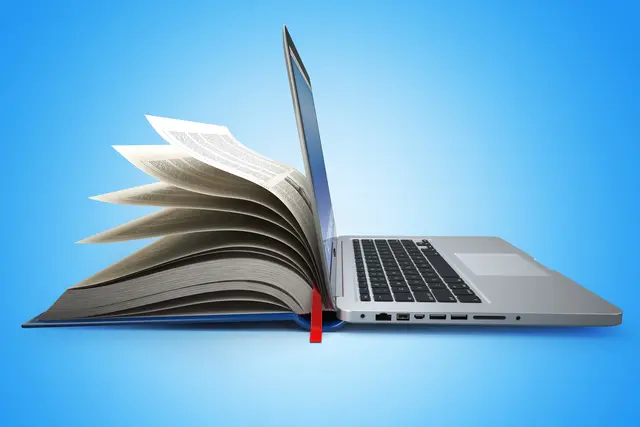 Laptop lehnt an aufgeschlagenes Buch