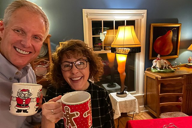 Prof. Travis und Karla Jensen lächeln in die Kamera und stoßen mit weihnachtlichen Tassen in der Hand an.