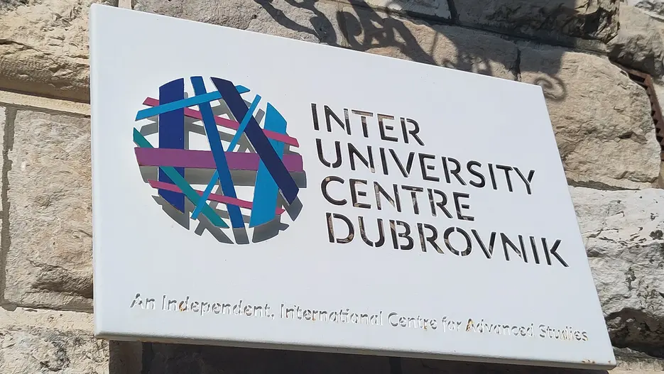 Schild des Inter-University Centre Dubrovnik an einer Steinmauer, mit buntem Logo und dem Zusatz „An Independent, International Centre for Advanced Studies“.