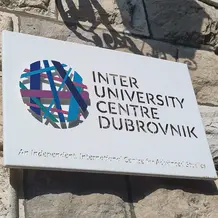 Schild des Inter-University Centre Dubrovnik an einer Steinmauer, mit buntem Logo und dem Zusatz „An Independent, International Centre for Advanced Studies“.