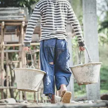 Kind schleppt schwere Eimer auf Baustelle