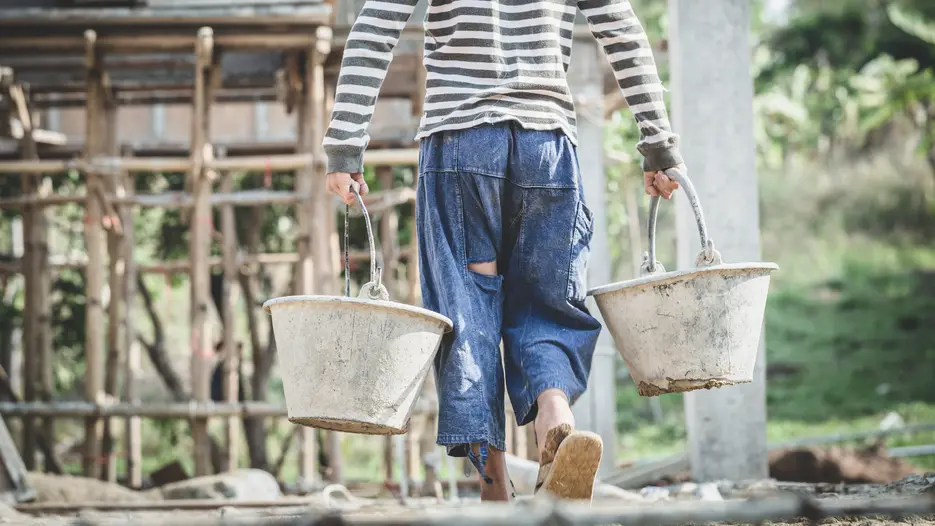 Kind schleppt schwere Eimer auf Baustelle