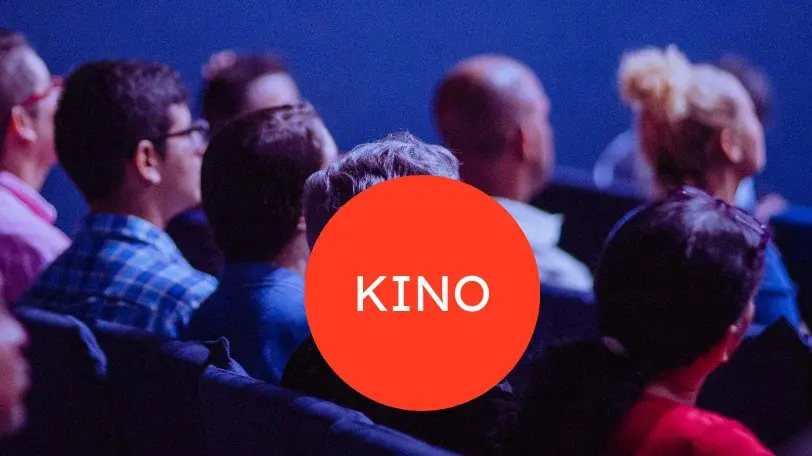 Im Hintergrund sieht man Kinopublikum, vorne ist ein roter Kreis zu sehen, in dessen Mitte in weißer Schrift "KINO" steht.