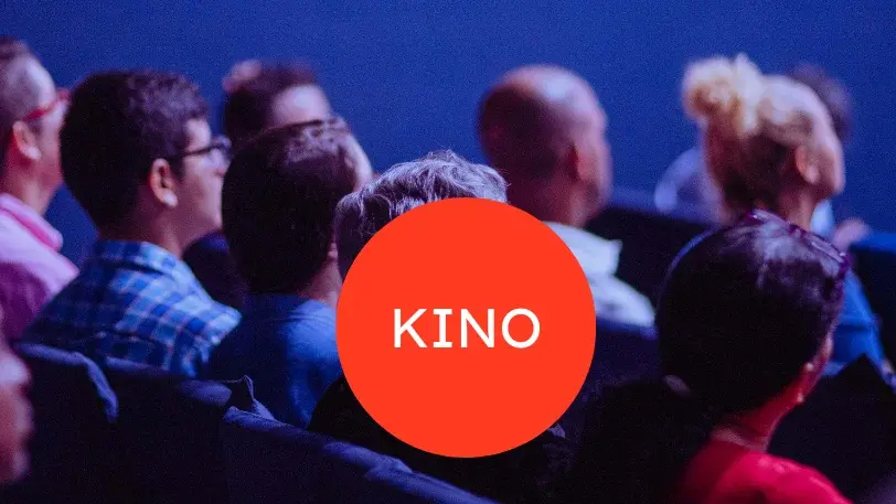 Im Hintergrund sieht man Kinopublikum, vorne ist ein roter Kreis zu sehen, in dessen Mitte in weißer Schrift "KINO" steht.