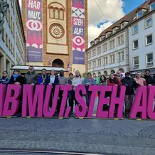 Die 16 teilnehmenden Studierenden mit Prof. Dr. Marievonne Sch&ouml;ttner, Dr. Tanja Grabovac und Prof. Dr. Katharina Karl (von links nach rechts) mit Katholikentagsmotto und Kiliansdom in W&uuml;rzburg